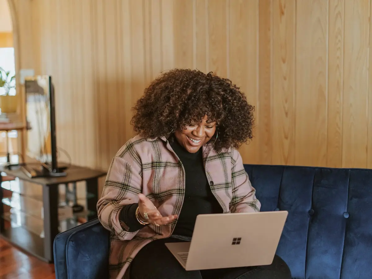 A woman on a sofa talking on her laptop, smiling.