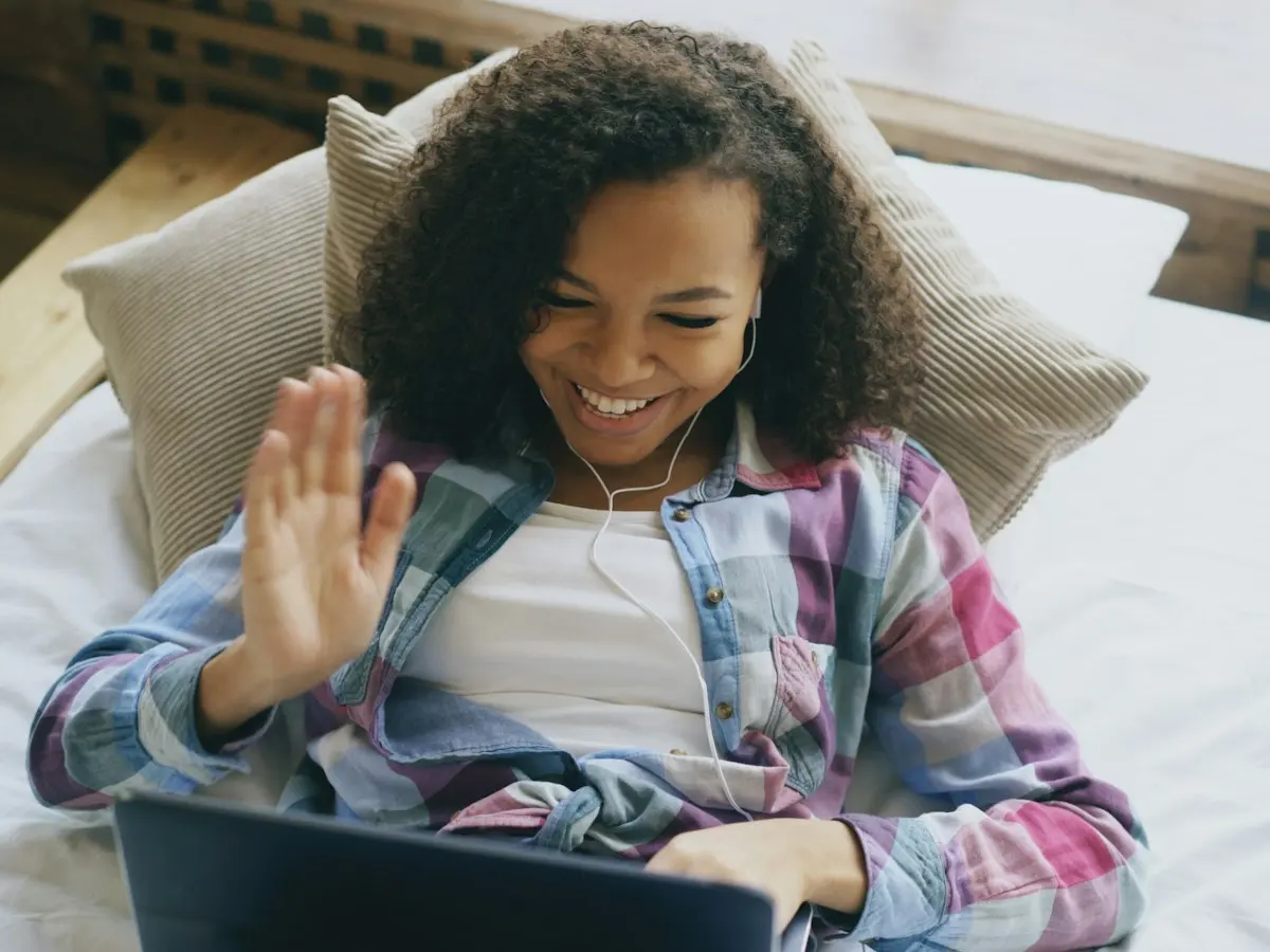 A woman waving hello on a video call.